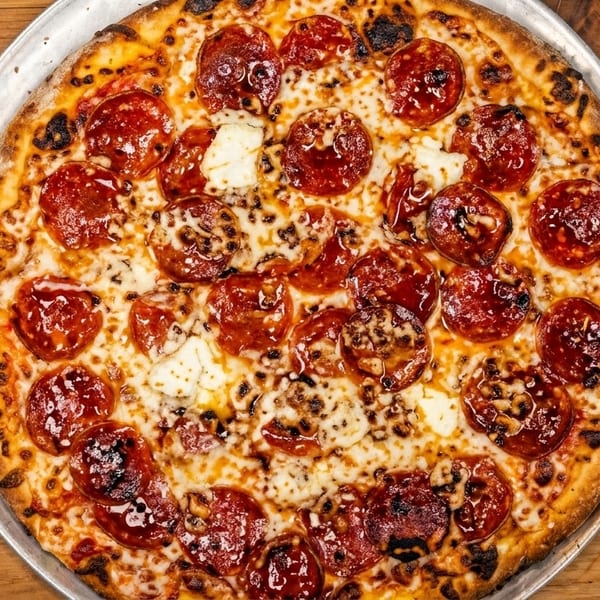 A whole pepperoni and cheese pizza on a metal pan, centered on a wooden table.