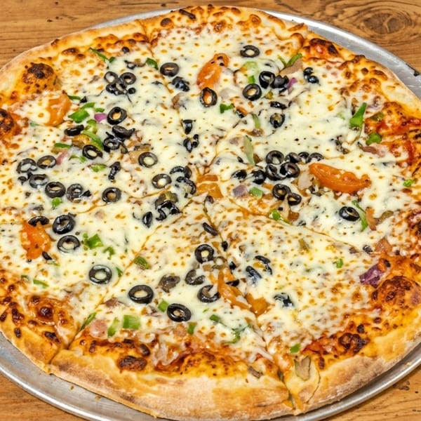 A whole pizza with black olives, green peppers, and melted cheese on a wooden table.